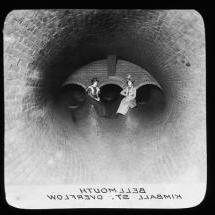 A historic picture of two women sitting in a brand new drainage pipe, circa 1898